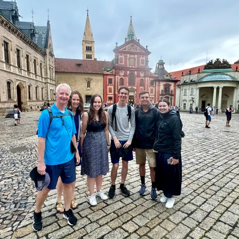 Travellers in a Prague Castle courtyard with the red facade of St George's Basilica behind them.