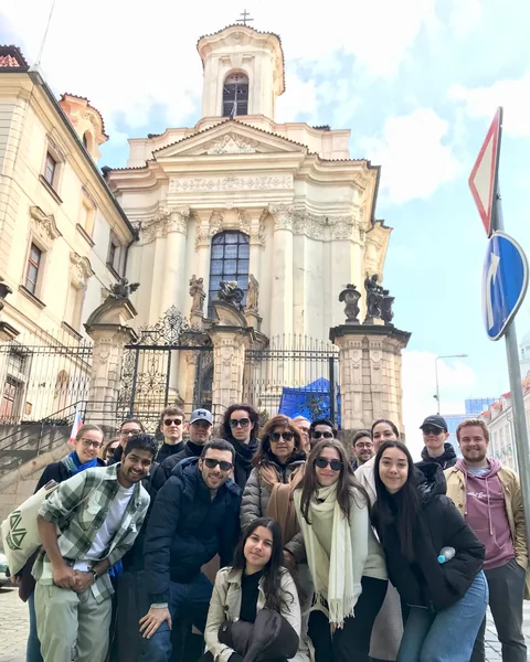Travellers gathered outside a church behind an ornate iron fence in Prague New Town.